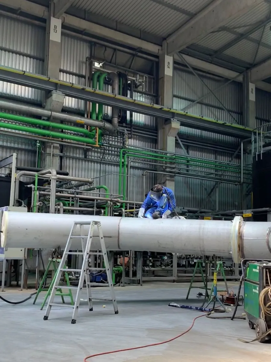 Mitarbeiter in blauer Arbeitskleidung an einem großen Rohrbauteil in der Halle